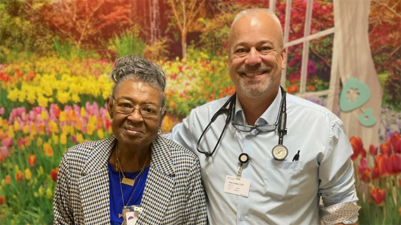 Participant and healthcare professional standing together in front of a floral mural.